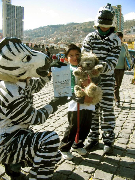 Bolivian Traffic Zebras La Paz - People dressed as zebras giving a kid holding a dog a present